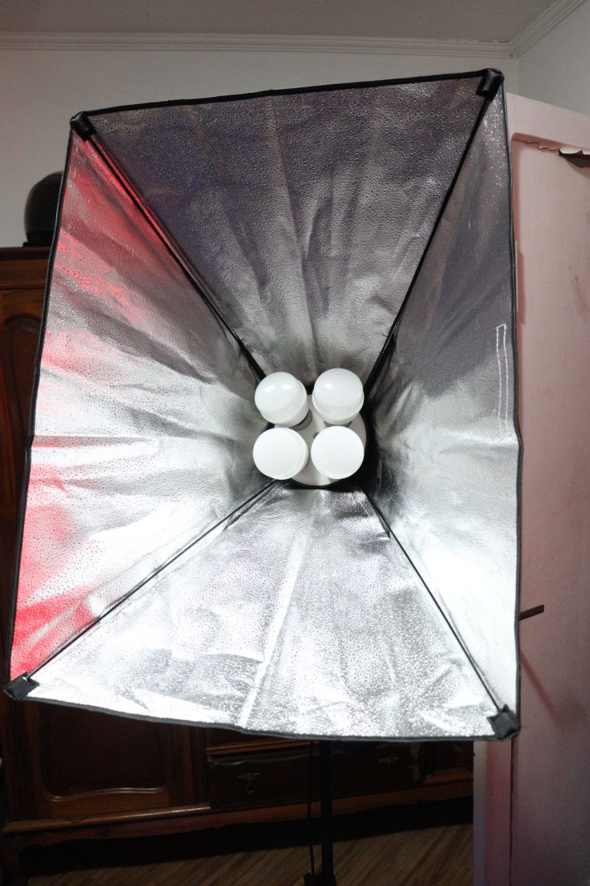 Picture of a pyramidal box made of cloth, seen from the rectangular side, silver on the 4 triangular insides, with 4 big light bulbs sticking from the back.