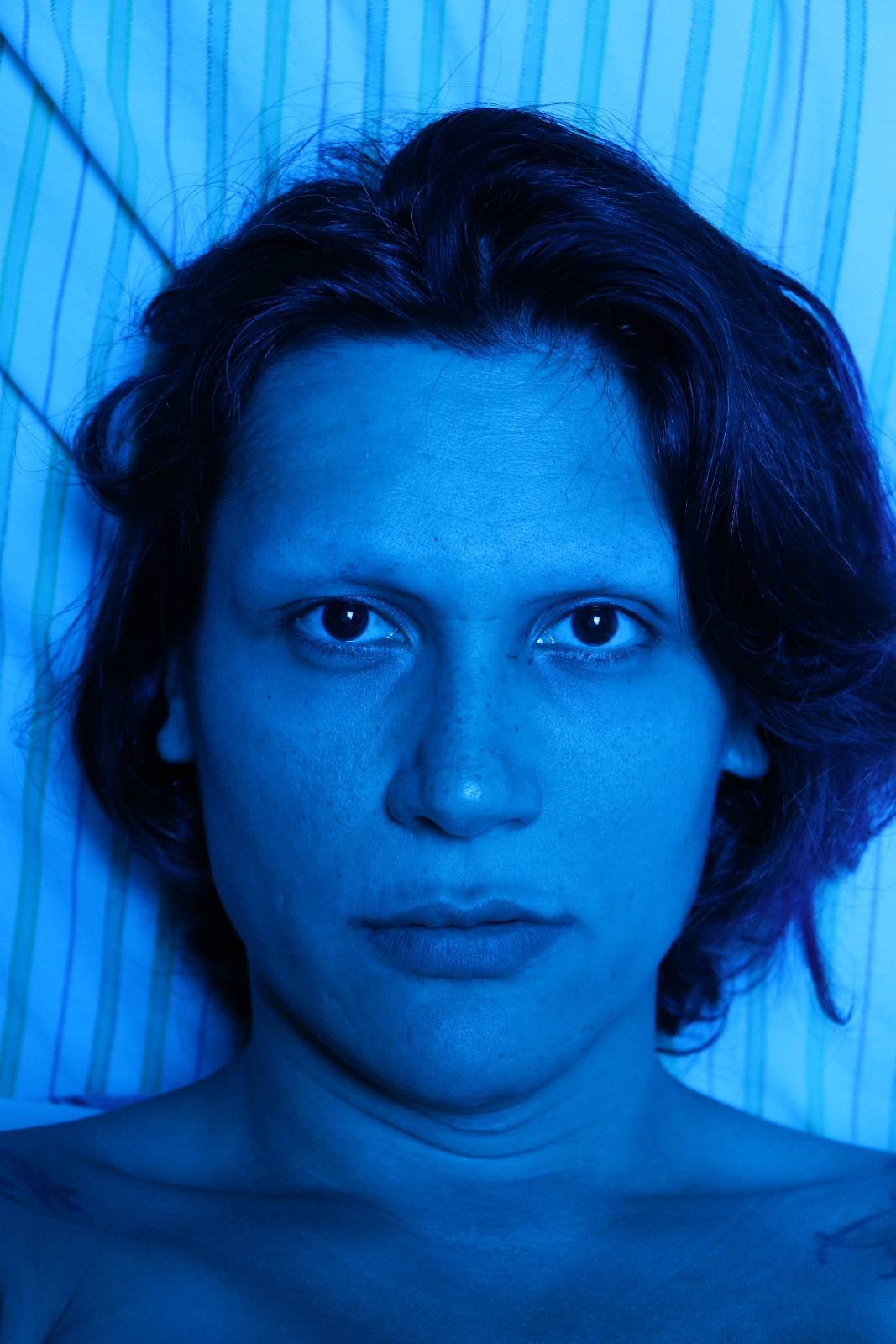 Picture of person's face lit by heavily saturated blue light. She has short black hair and black eyes